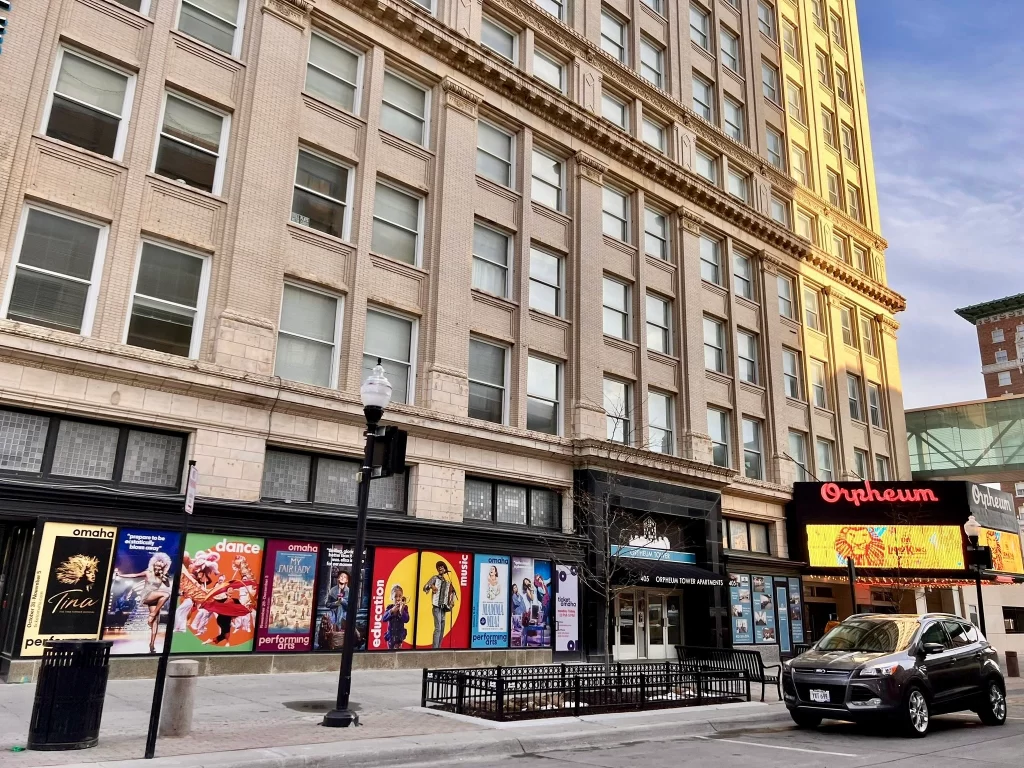 Photo of a light brown historic building with theatre posters lining the walls