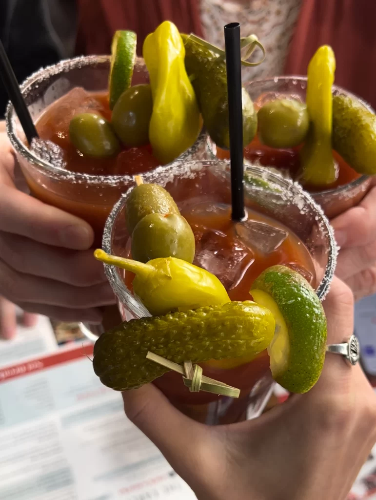 three hands holding bloody mary drinks cheersing