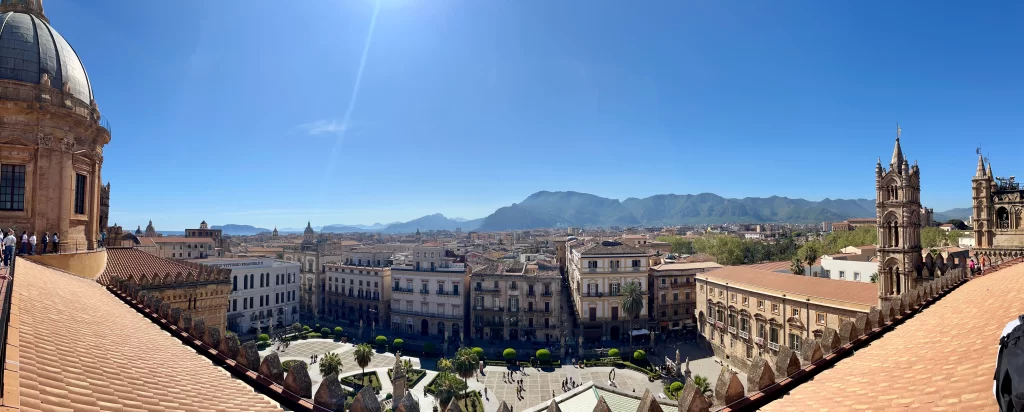 Rooftop view overlooking a square below and a sunny day with a blue sky and view of the mountains