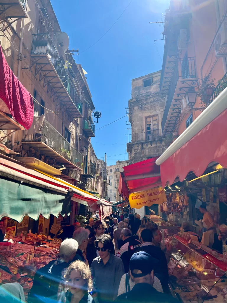 Colorful outdoor market stalls on either side of the street with people walking through