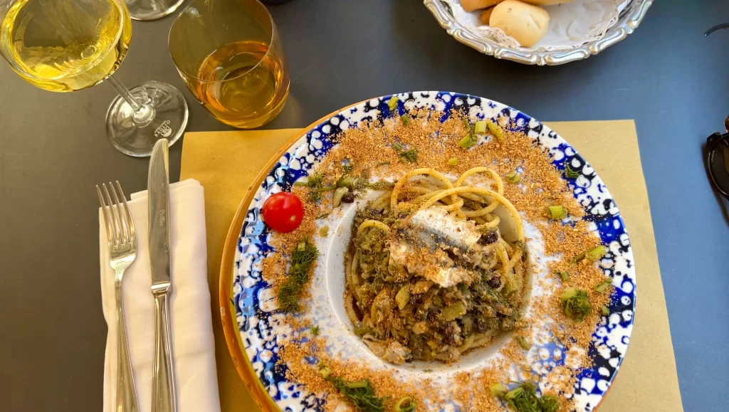 View of a pasta with sardines dish from above with a glass of white wine on the left