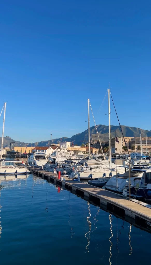 View of Port of Palermo with sailboats next to a doc and mountains in the distance