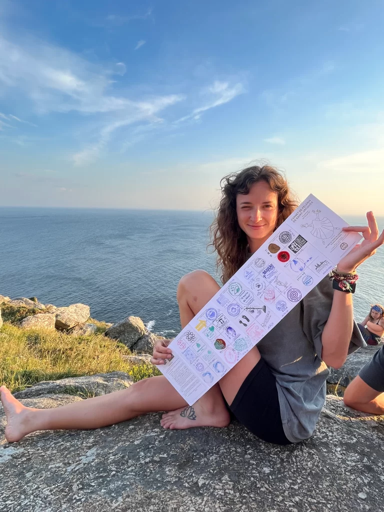 Woman sitting on a cliff holding a stamped piece of paper and winking