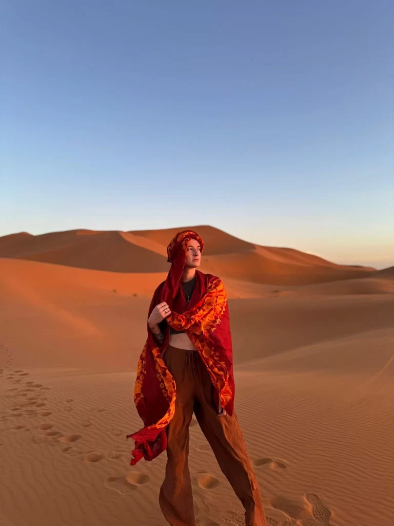 Woman standing in the Sahara desert with a red cloth draped around her